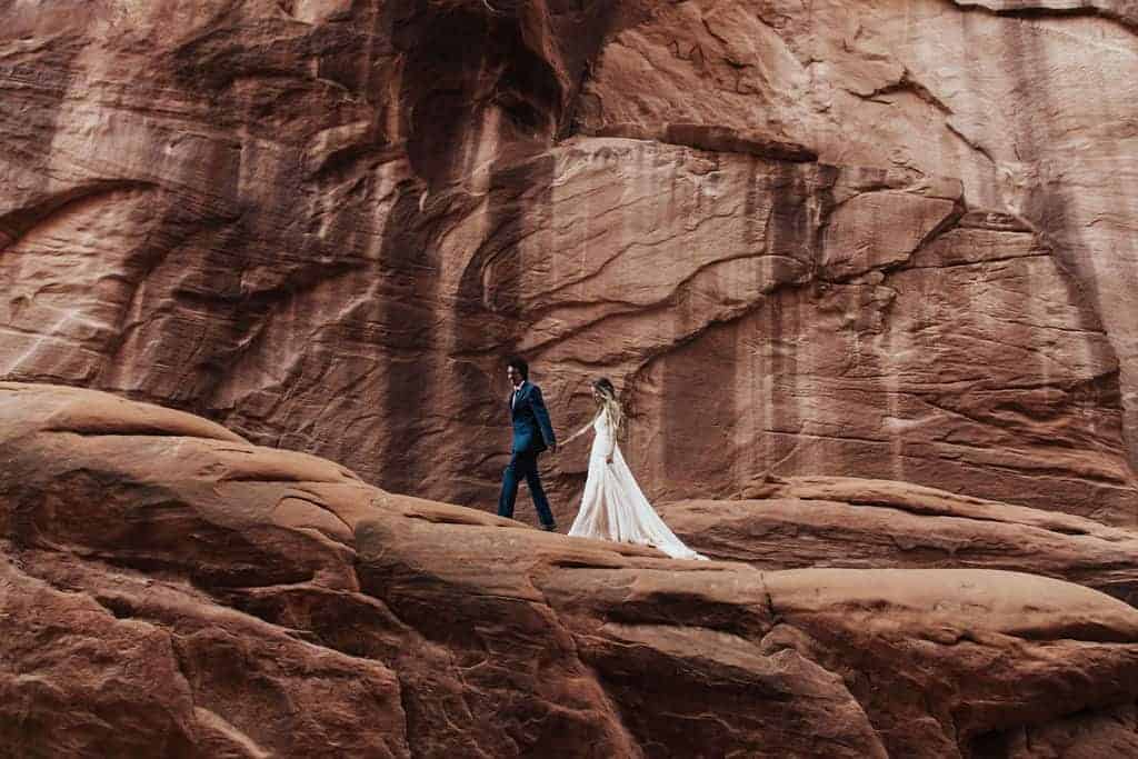 Couple walking on edge near Sand Dune Arch at Arches National Park before their low-key Sand Dune Arch elopement | Nicole Aston Photography | Zion Brides