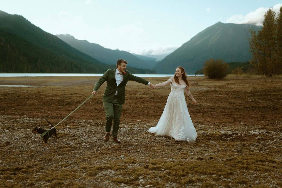Couple running next to a Washington lake with their dog | Rainy Intimate Wedding in Washington State | Emilee Setting | Adventure Wed Feature
