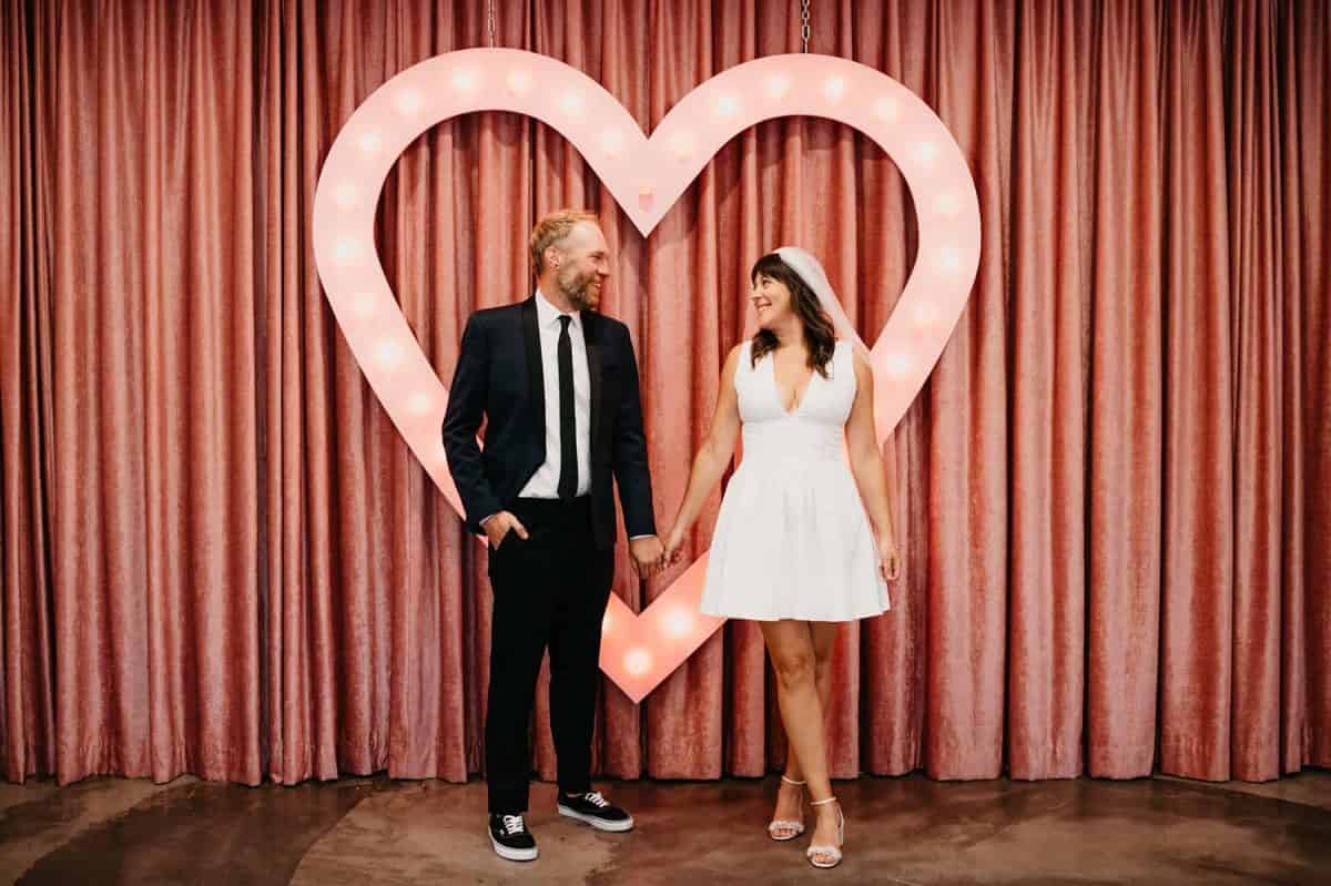 Couple sharing vow renewal ceremony in front of heart and curtains | Sure Thing Chapel Ten-Year Anniversary Vow Renewal | Amber Garrett Photography | Adventure Wed Feature